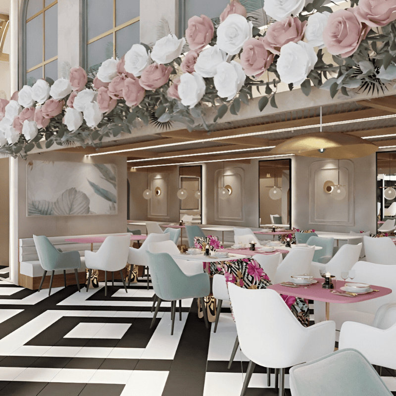 A beautifully decorated café interior featuring pastel-colored chairs, pink table settings, and a floral arrangement of white and blush roses hanging above, with a modern black-and-white tiled floor.